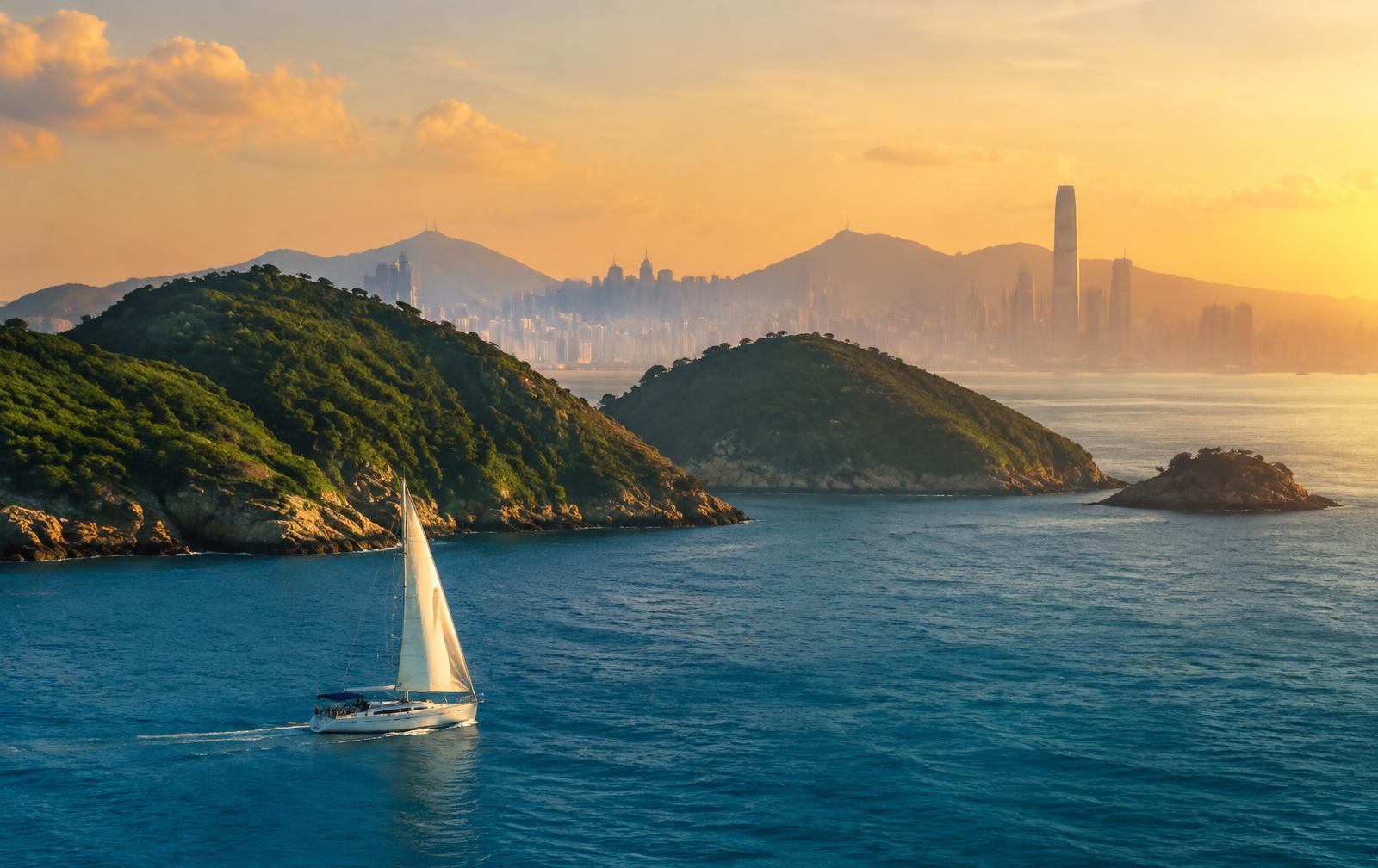 Sailing yacht cruising past the outlying islands of Hong Kong with the city skyline beyond